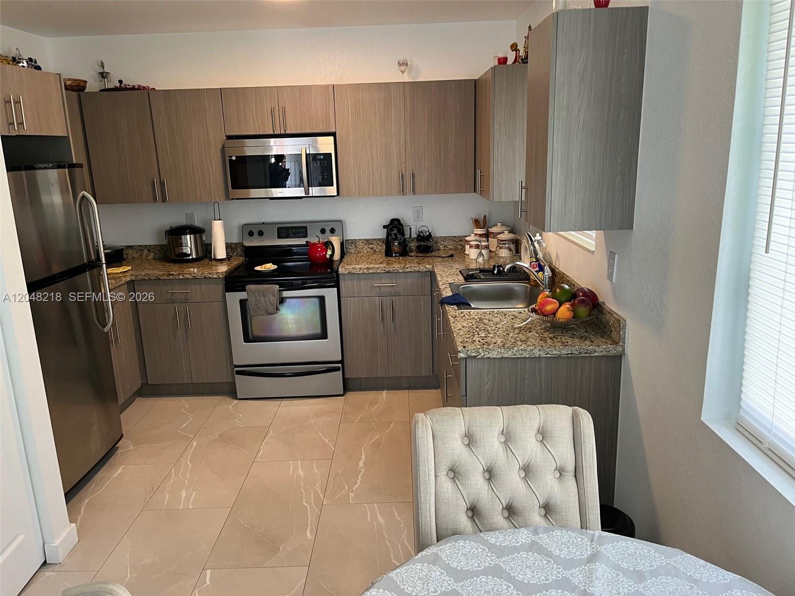 A kitchen features wood-grain cabinets, stainless steel appliances, and granite countertops over tiled floors — 10235 SW 173rd St # 10235, Miami FL 33157, MIAMI, FL