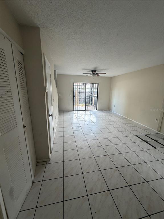 An empty living room features white tiled floors, a ceiling fan, and sliding glass doors — 5861 CURRY FORD ROAD UNIT 12, ORLANDO, FL