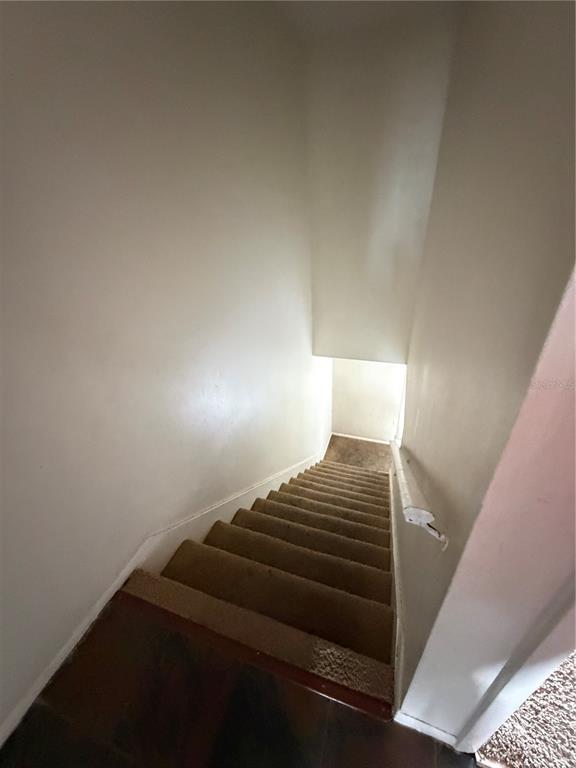 A carpeted staircase descends between two plain, light-colored walls with a white handrail — 5861 CURRY FORD ROAD UNIT 12, ORLANDO, FL