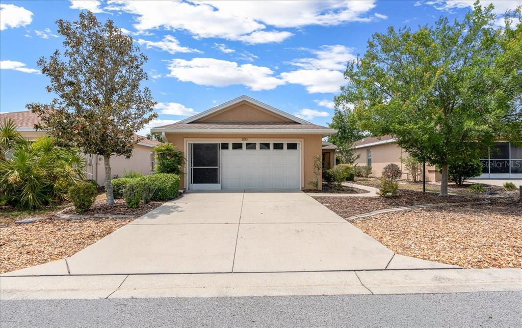 A tan single-story house features a two-car garage, a concrete driveway, and landscaped front yard — 9183 SW 102ND CIRCLE, OCALA, FL