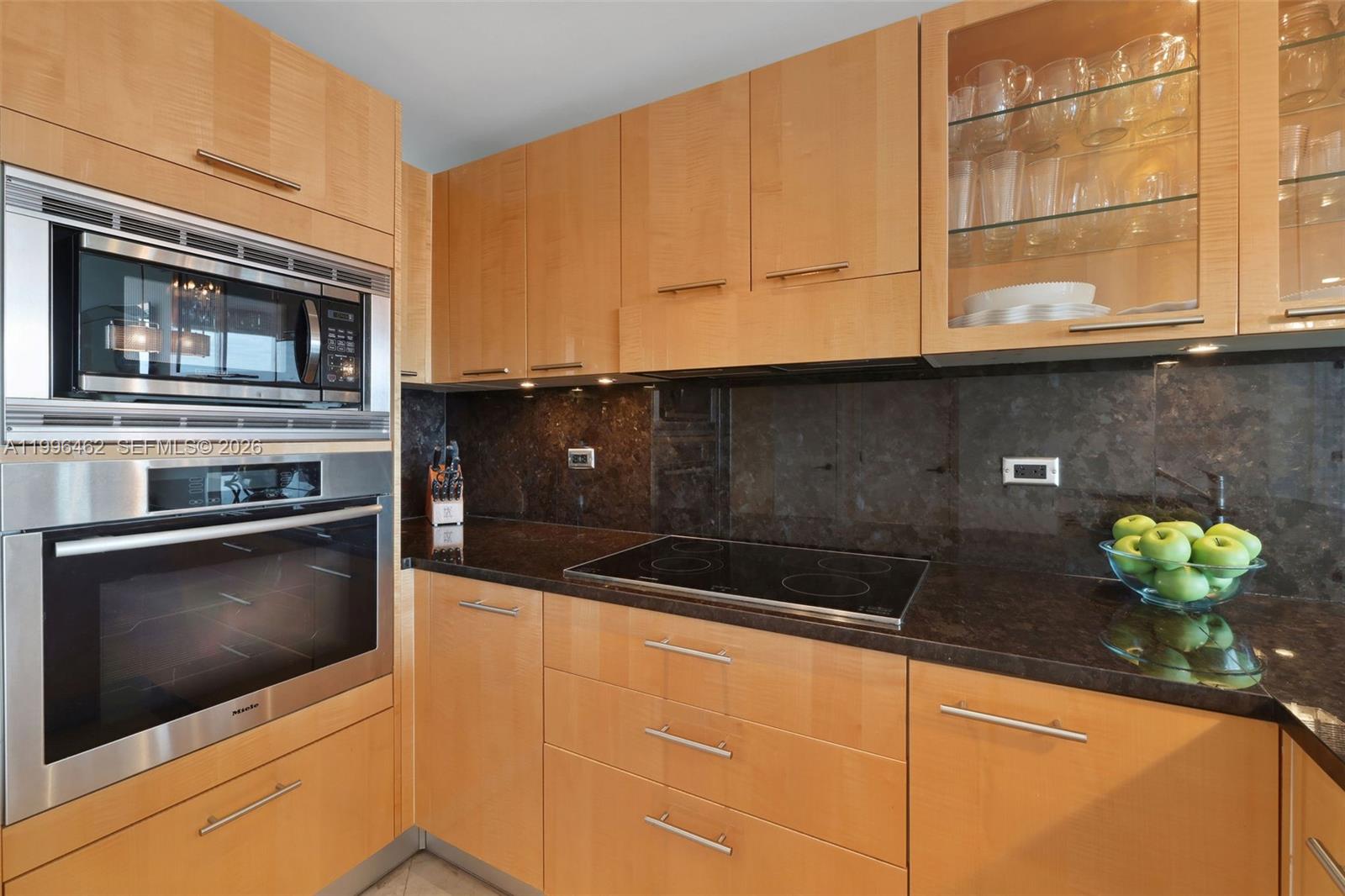 A kitchen features light wood cabinets, a dark stone countertop, and stainless steel appliances — 6799 Collins Ave # 1106, Miami Beach FL 33141, MIAMI BEACH, FL