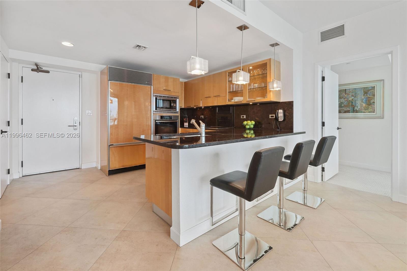 A kitchen features light wood cabinets, a dark granite island, and three black bar stools — 6799 Collins Ave # 1106, Miami Beach FL 33141, MIAMI BEACH, FL