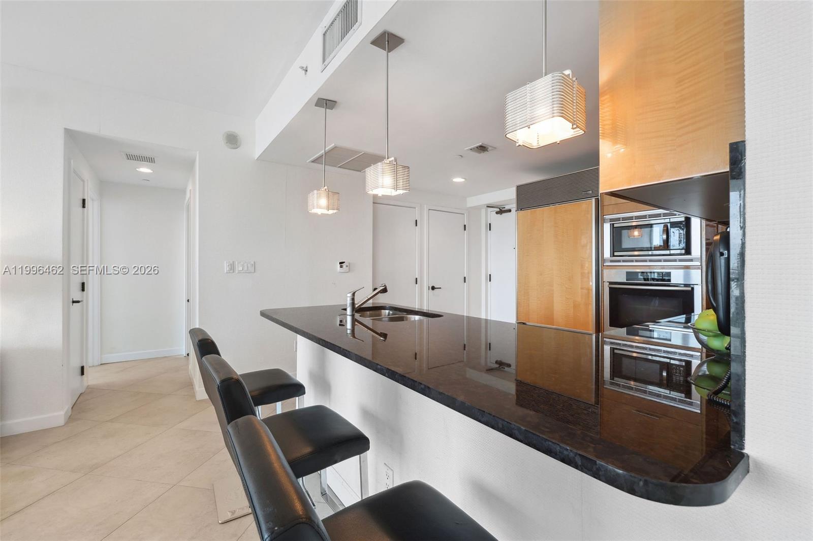 A kitchen features a dark granite breakfast bar, black stools, and stainless steel appliances — 6799 Collins Ave # 1106, Miami Beach FL 33141, MIAMI BEACH, FL