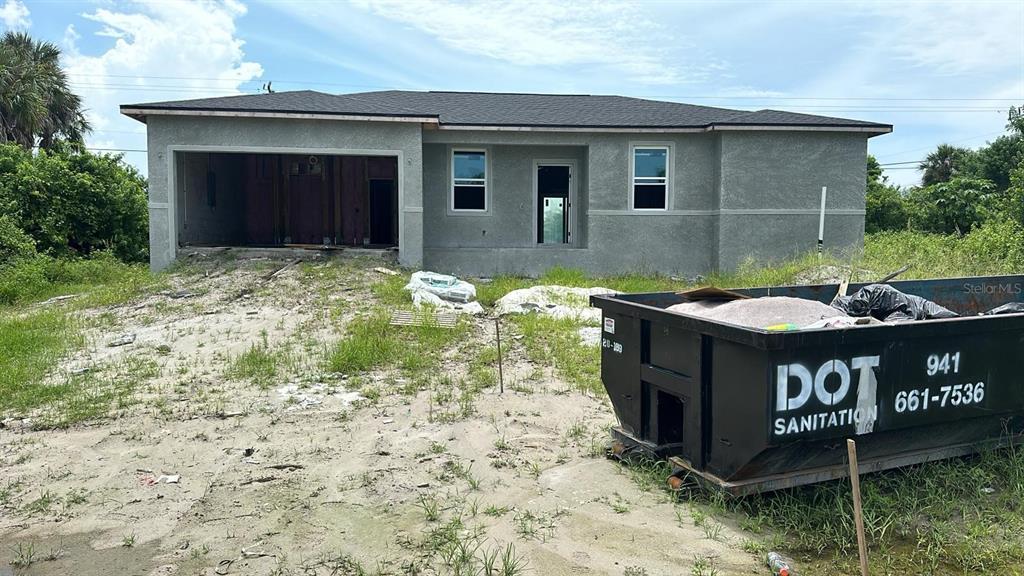 A single-story house under construction features a garage opening and a large dumpster in front — 18581 LAKE WORTH BOULEVARD, PORT CHARLOTTE, FL