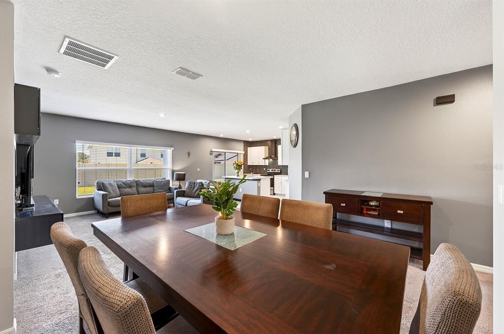 A dining area with a dark wood table and chairs opens into a living room — 596 MEADOW BEND DRIVE, DAVENPORT, FL