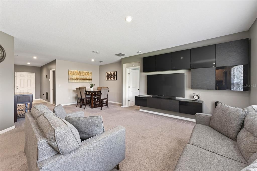 A living room features gray carpet, a large television, black wall cabinetry, and dining furniture — 596 MEADOW BEND DRIVE, DAVENPORT, FL