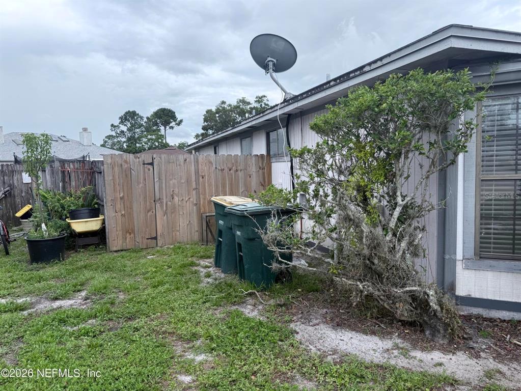 A side view of a house exterior with a wooden fence, trash bins, and landscaping — 2288 IRONSTONE DRIVE E, JACKSONVILLE, FL