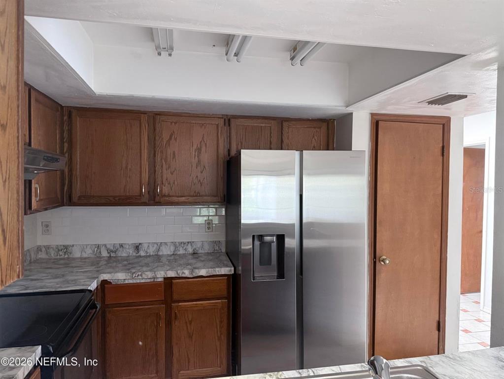 A kitchen features wood cabinets, a stainless steel refrigerator, and marble-patterned countertops — 2288 IRONSTONE DRIVE E, JACKSONVILLE, FL
