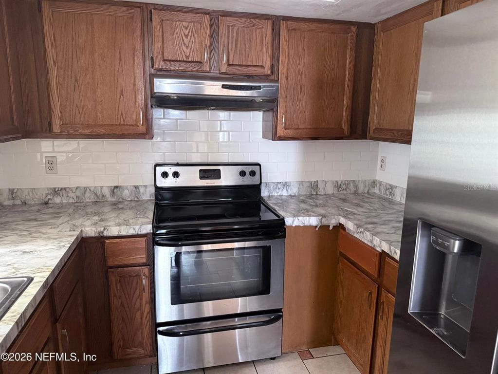 A kitchen features wood cabinets, a stainless steel stove, and marble-patterned laminate countertops — 2288 IRONSTONE DRIVE E, JACKSONVILLE, FL