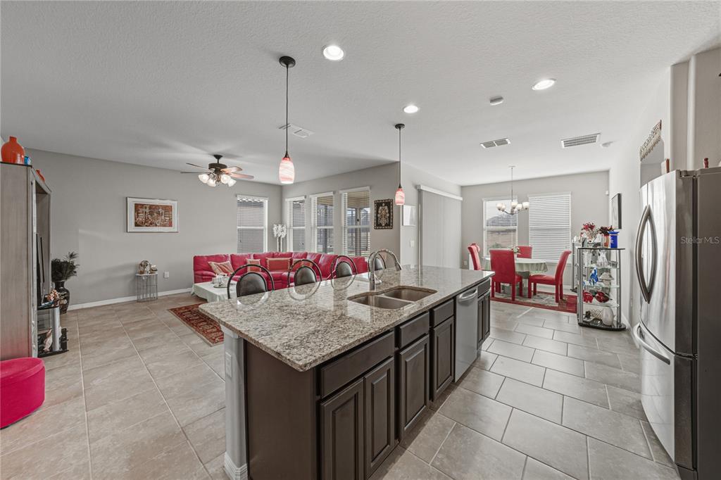 An open-concept kitchen with a granite island overlooks a living area and dining space — 4169 PRIMA LAGO CIRCLE, LAKELAND, FL