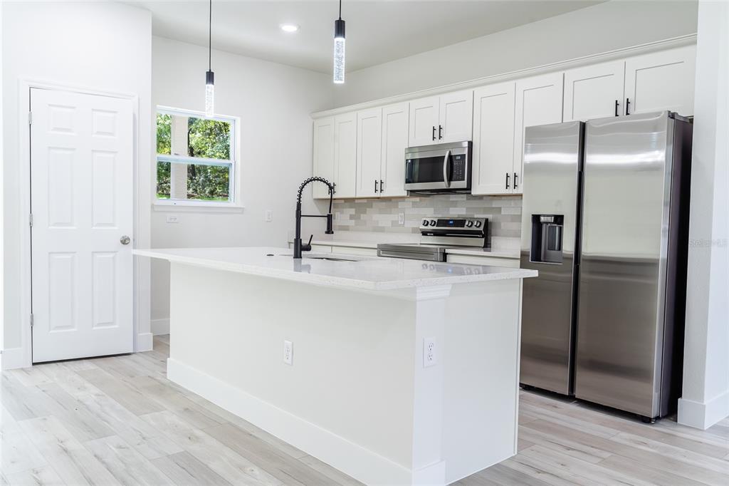 A modern kitchen features white cabinets, stainless steel appliances, a quartz island, and light flooring — 10955 N DRAGONIS DRIVE, CITRUS SPRINGS, FL
