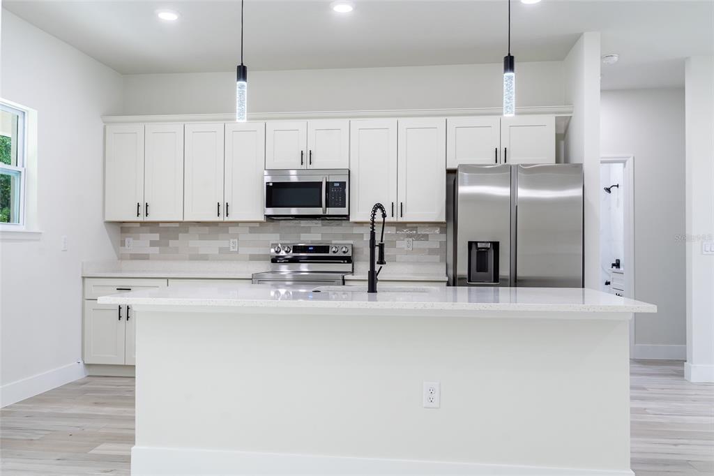 A modern kitchen features white cabinets, stainless steel appliances, a quartz island, and pendant lighting — 10955 N DRAGONIS DRIVE, CITRUS SPRINGS, FL