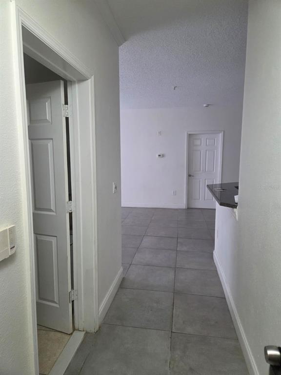 A hallway with gray tile flooring leads to an open living area with white walls — 5536 METROWEST BOULEVARD UNIT 8-109, ORLANDO, FL