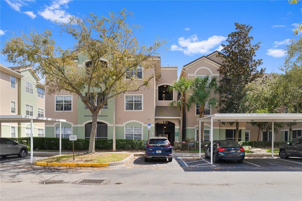 A three-story apartment building with covered parking spaces and trees in the foreground — 4833 CYPRESS WOODS DRIVE UNIT 4114, ORLANDO, FL