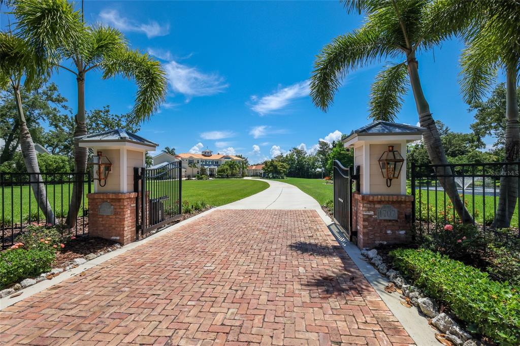 A brick driveway leads through an open gate toward a large house with palm trees — 1707 71ST STREET NW, BRADENTON, FL