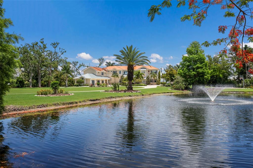 A large house with a red roof sits behind a pond with a fountain — 1707 71ST STREET NW, BRADENTON, FL