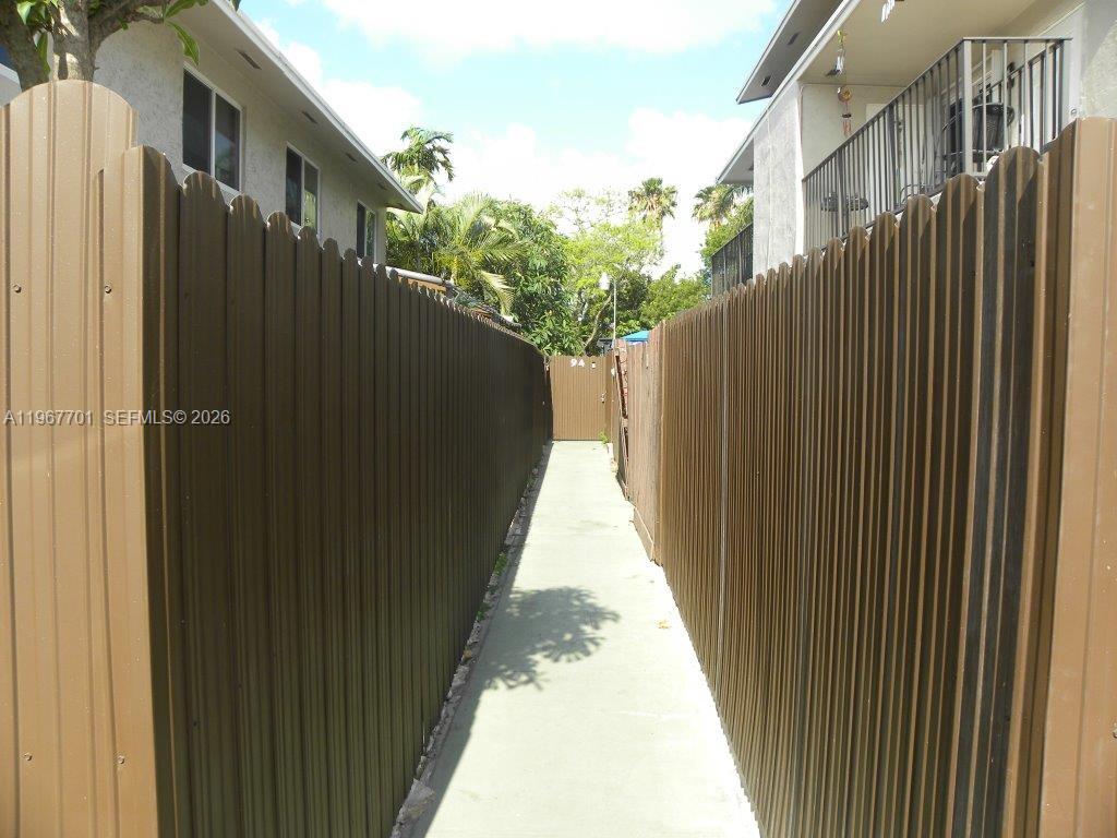 A narrow concrete walkway is enclosed by tall brown privacy fences between two buildings — 15690 SW 82nd Cir Ln # 1, Miami FL 33193, MIAMI, FL