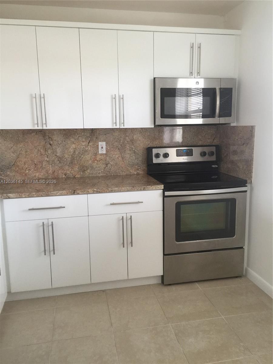 A kitchen features white cabinets, stainless steel appliances, and a brown stone-look backsplash — 7722 Camino Real # 415, Miami FL 33143, MIAMI, FL