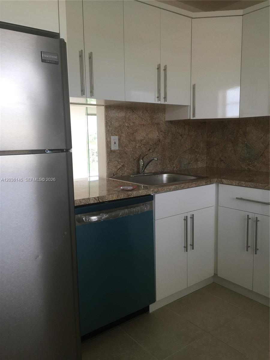 A kitchen features white cabinets, a stainless steel refrigerator, a dishwasher, and stone countertops — 7722 Camino Real # 415, Miami FL 33143, MIAMI, FL