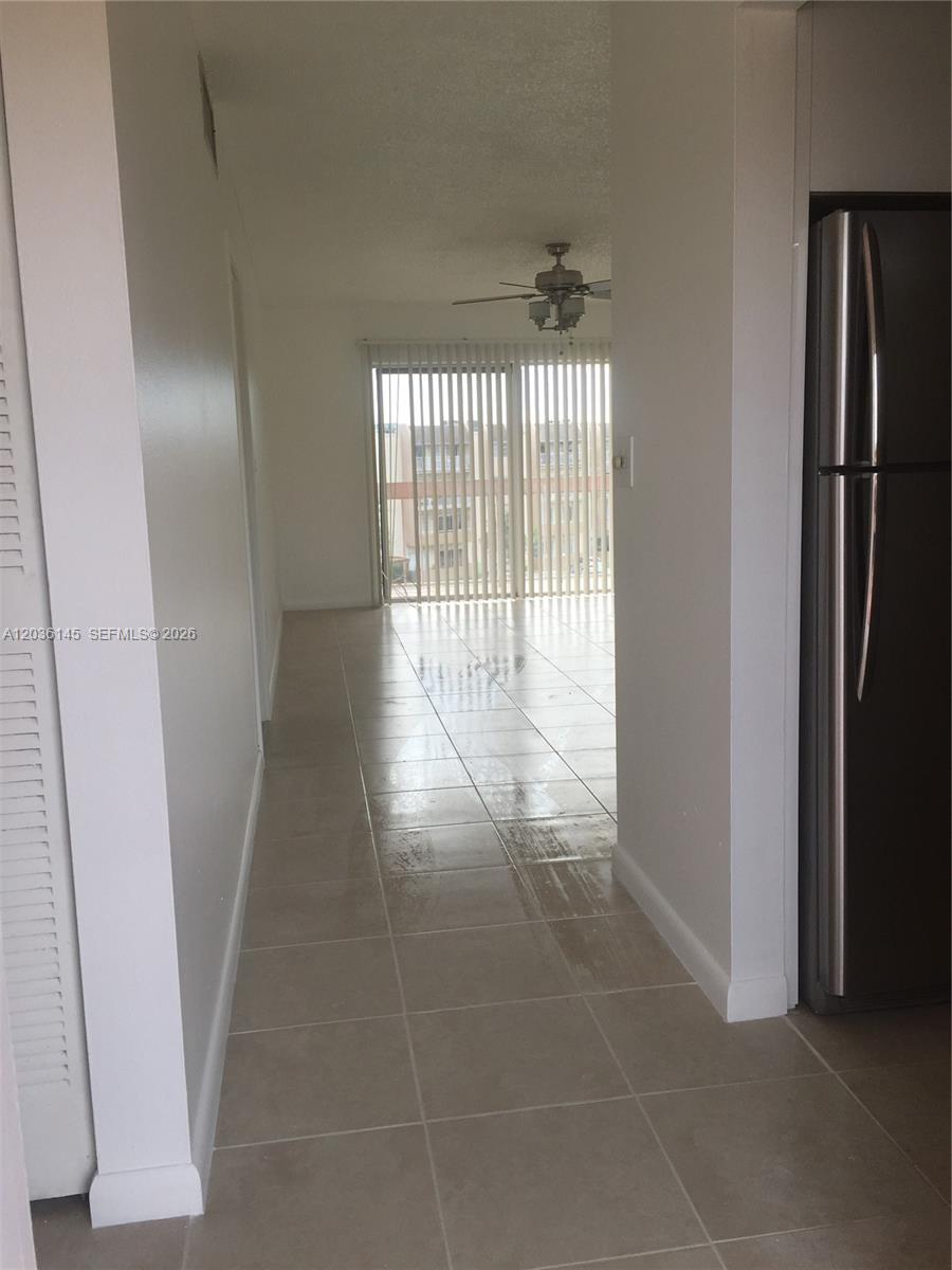 A tiled hallway leads to a living area with a ceiling fan and sliding glass doors — 7722 Camino Real # 415, Miami FL 33143, MIAMI, FL