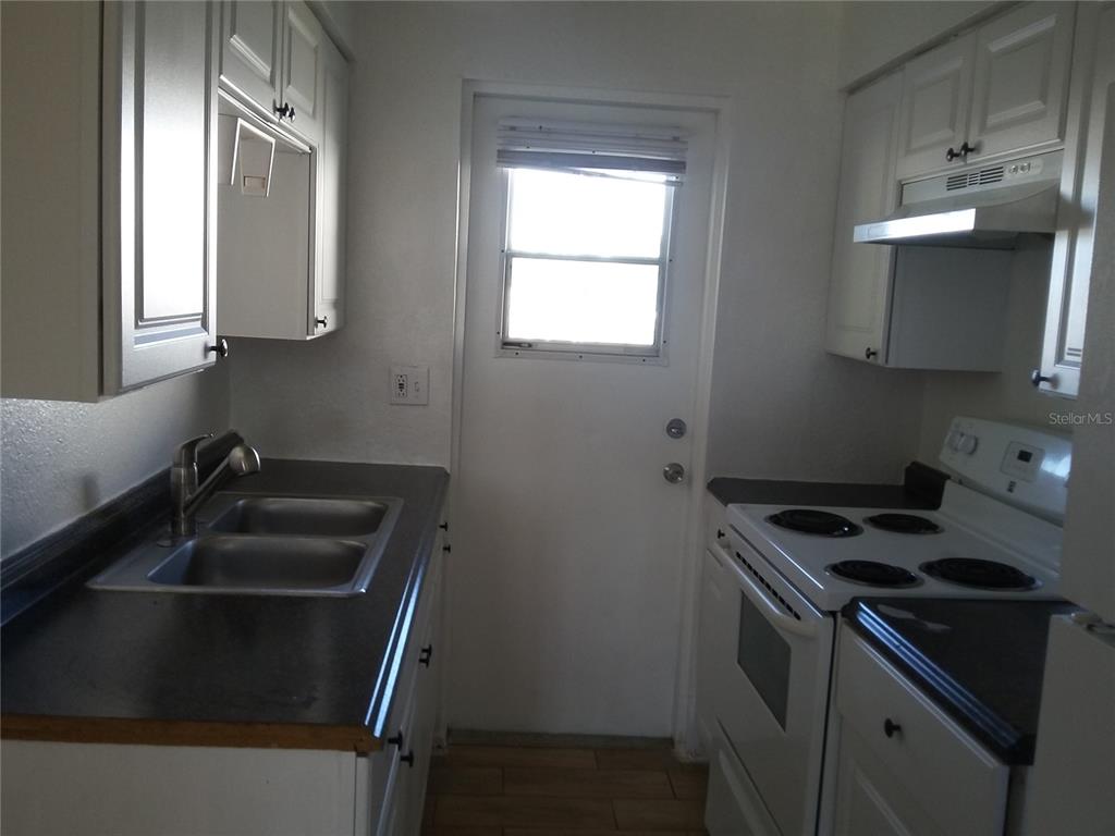 A galley kitchen features white cabinets, dark countertops, a double sink, and a white stove — 1710 S WASHINGTON AVENUE UNIT 06, TITUSVILLE, FL