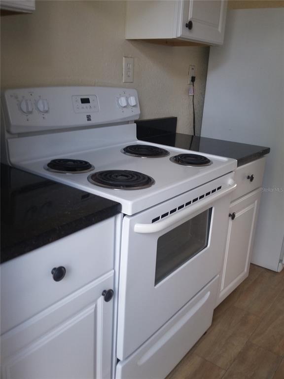 A white electric range sits between white cabinets with black countertops in a kitchen — 1710 S WASHINGTON AVENUE UNIT 06, TITUSVILLE, FL