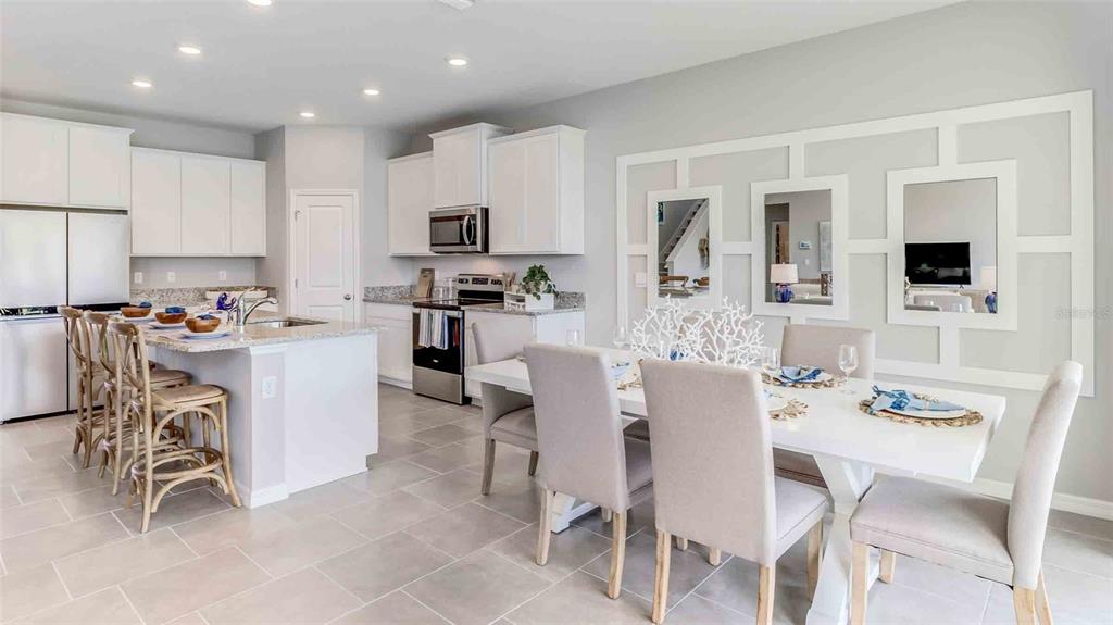 A bright kitchen and dining area featuring white cabinetry, granite countertops, and a paneled wall — 36283 HILLRIDGE TRAIL, ZEPHYRHILLS, FL
