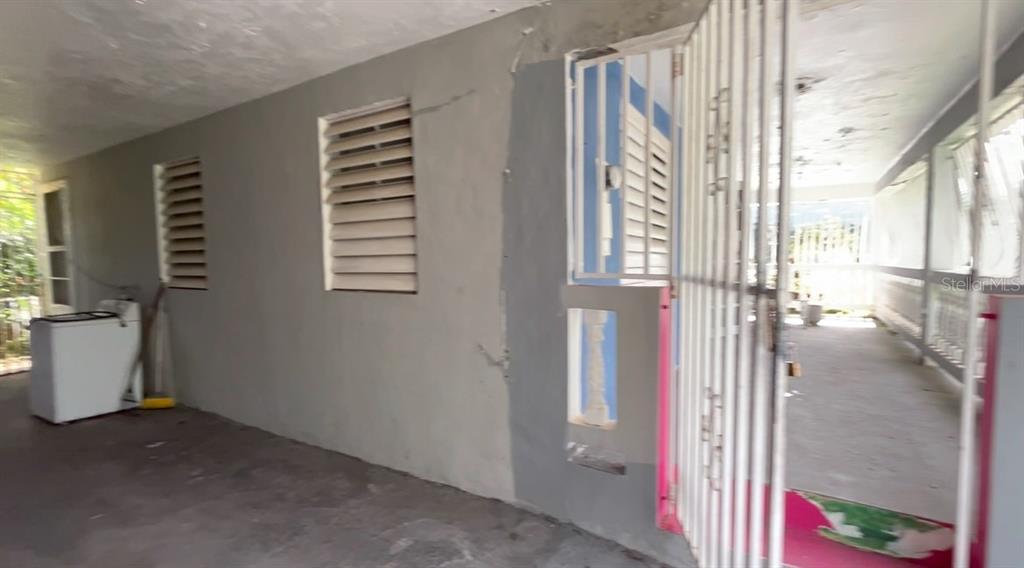 A covered outdoor patio area features a washing machine, louvered windows, and a metal gate — 233 Bo Cienaga Alta MALPICA, RIO GRANDE, PR
