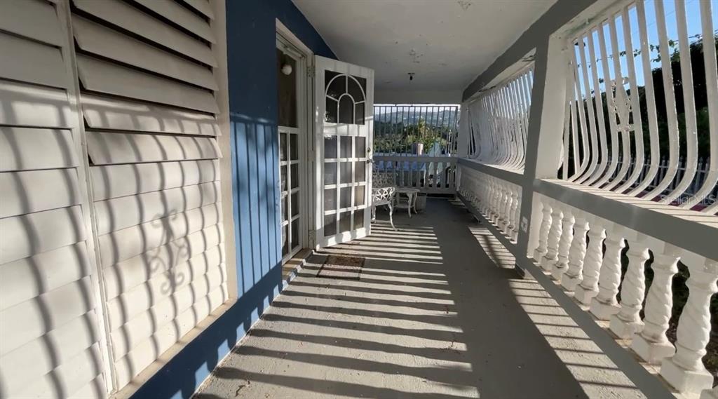 A covered balcony features a blue wall, white louvered shutters, and a white balustrade railing — 233 Bo Cienaga Alta MALPICA, RIO GRANDE, PR
