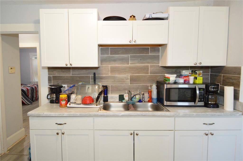 A kitchen features white cabinets, a gray wood-look tile backsplash, and a stainless steel sink — 2351 25TH AVENUE S, ST PETERSBURG, FL