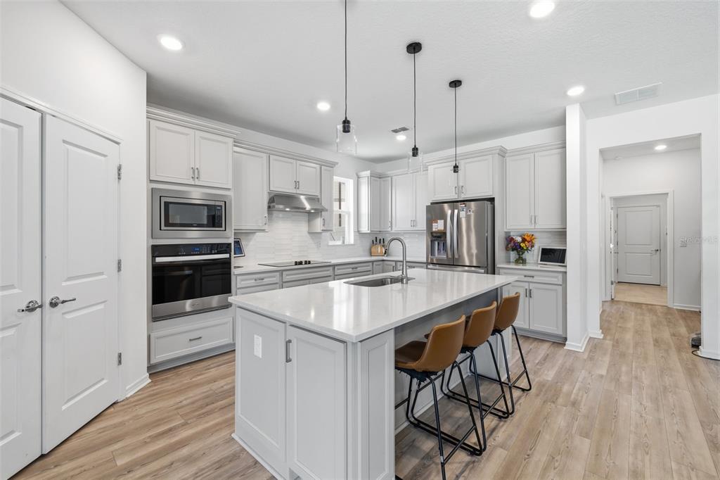 A modern kitchen features light gray cabinetry, a large white island, and stainless steel appliances — 12071 ORCHID ASH STREET, RIVERVIEW, FL