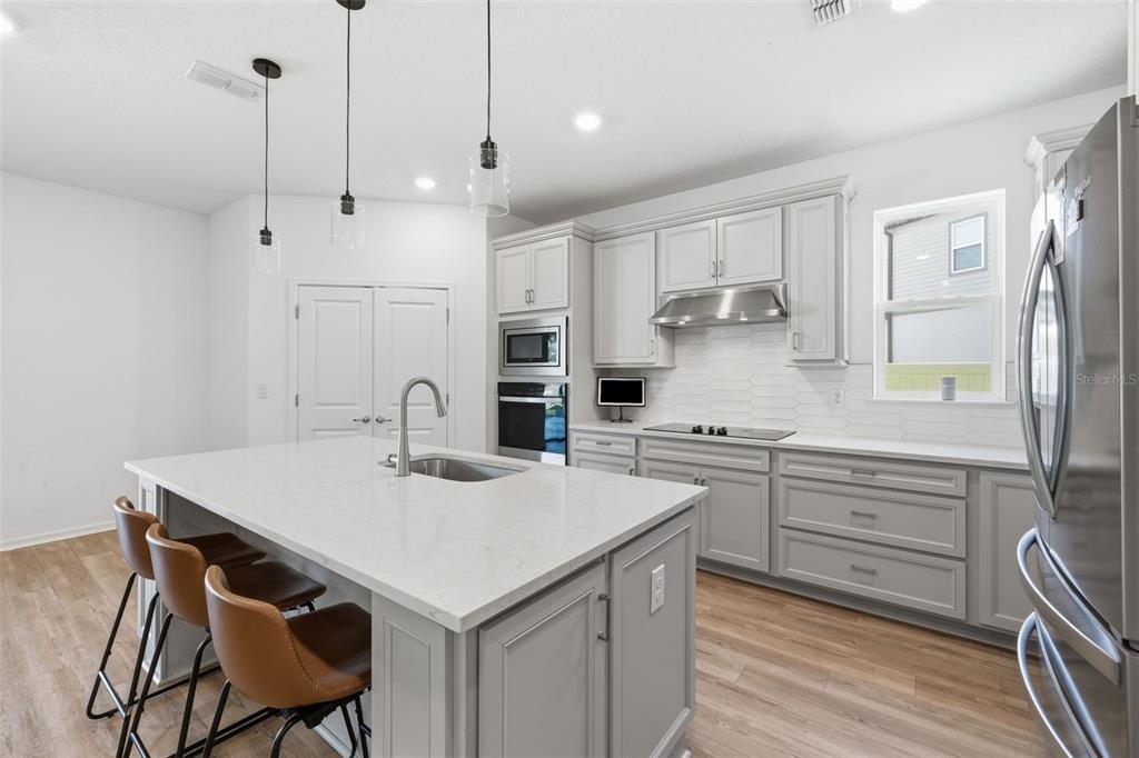 A modern kitchen features light gray cabinets, a white quartz island, and three pendant lights — 12071 ORCHID ASH STREET, RIVERVIEW, FL