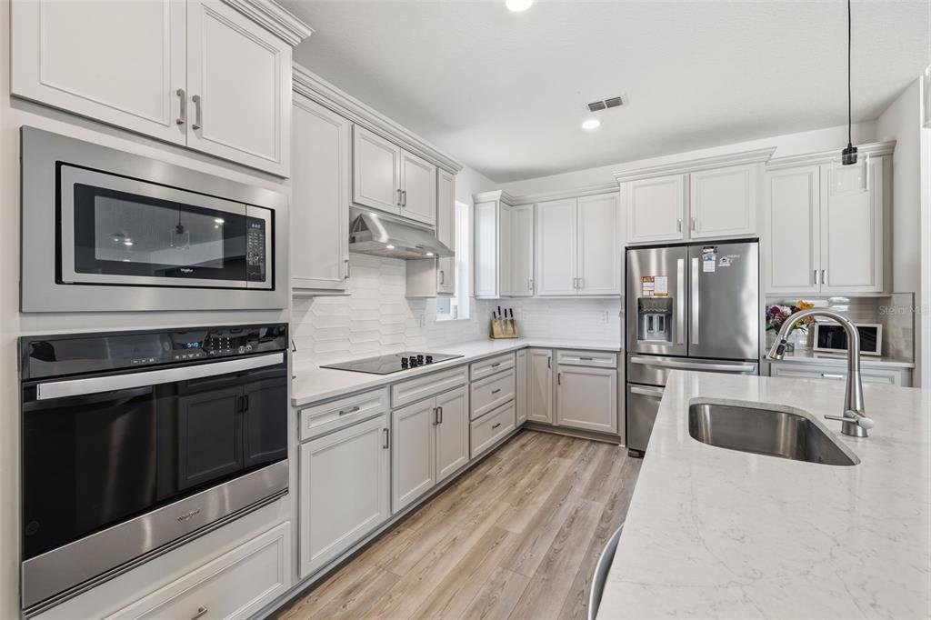 A modern kitchen features light gray cabinets, stainless steel appliances, and a white quartz island — 12071 ORCHID ASH STREET, RIVERVIEW, FL