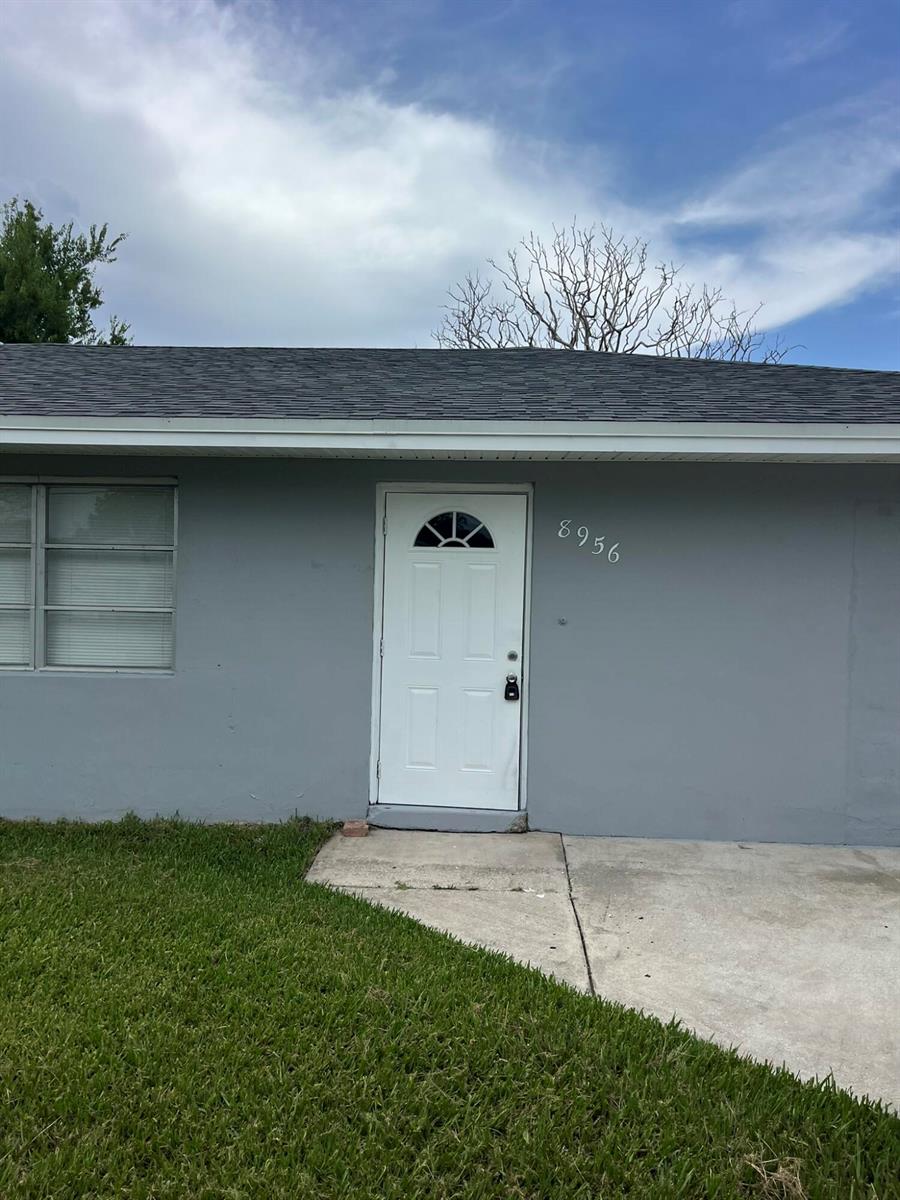 A gray house exterior features a white front door with a small arched window — 8956 SE 65th Way, Okeechobee FL 34974, OKEECHOBEE, FL