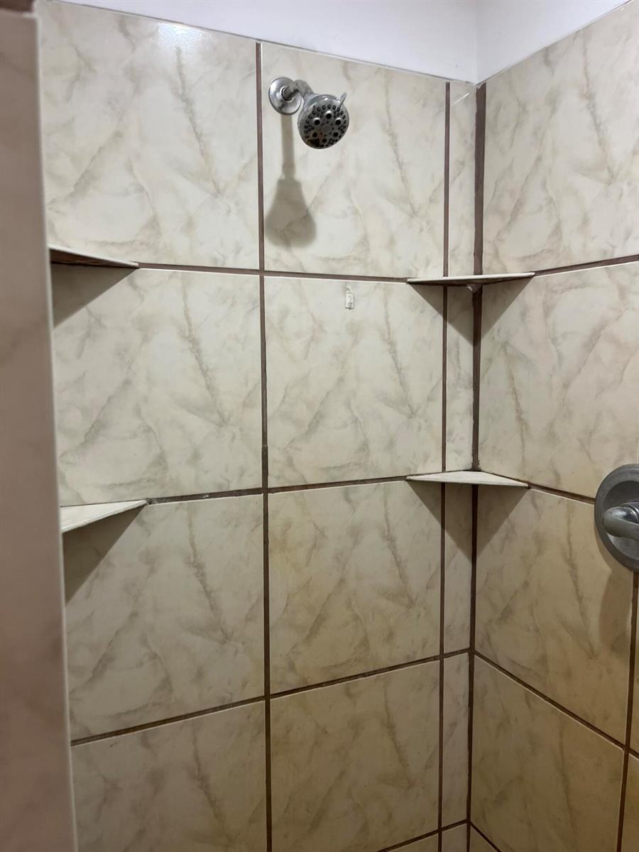 A shower stall with beige marble-patterned tiles, a chrome showerhead, and three built-in corner shelves — 8956 SE 65th Way, Okeechobee FL 34974, OKEECHOBEE, FL