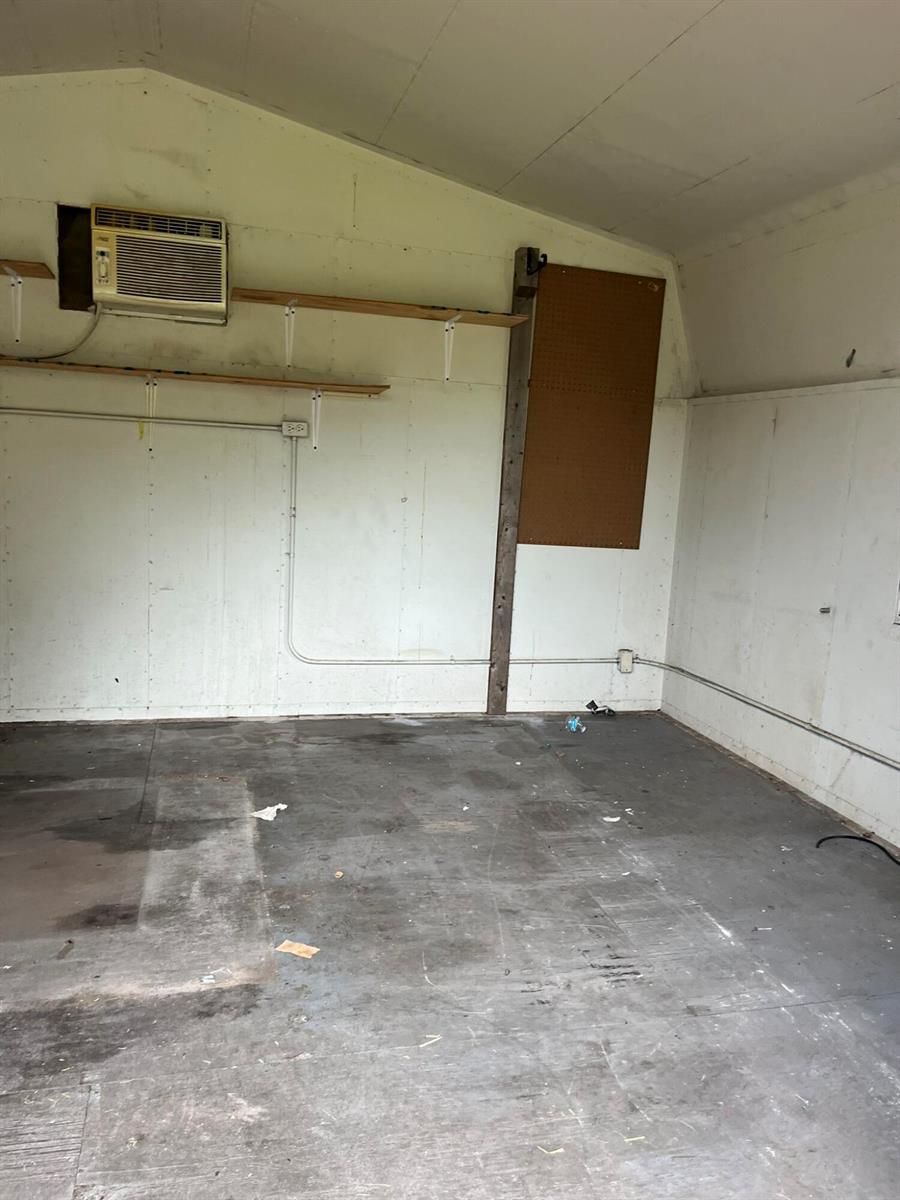 An interior view of a shed featuring white walls, a window air conditioner, and shelving — 8956 SE 65th Way, Okeechobee FL 34974, OKEECHOBEE, FL