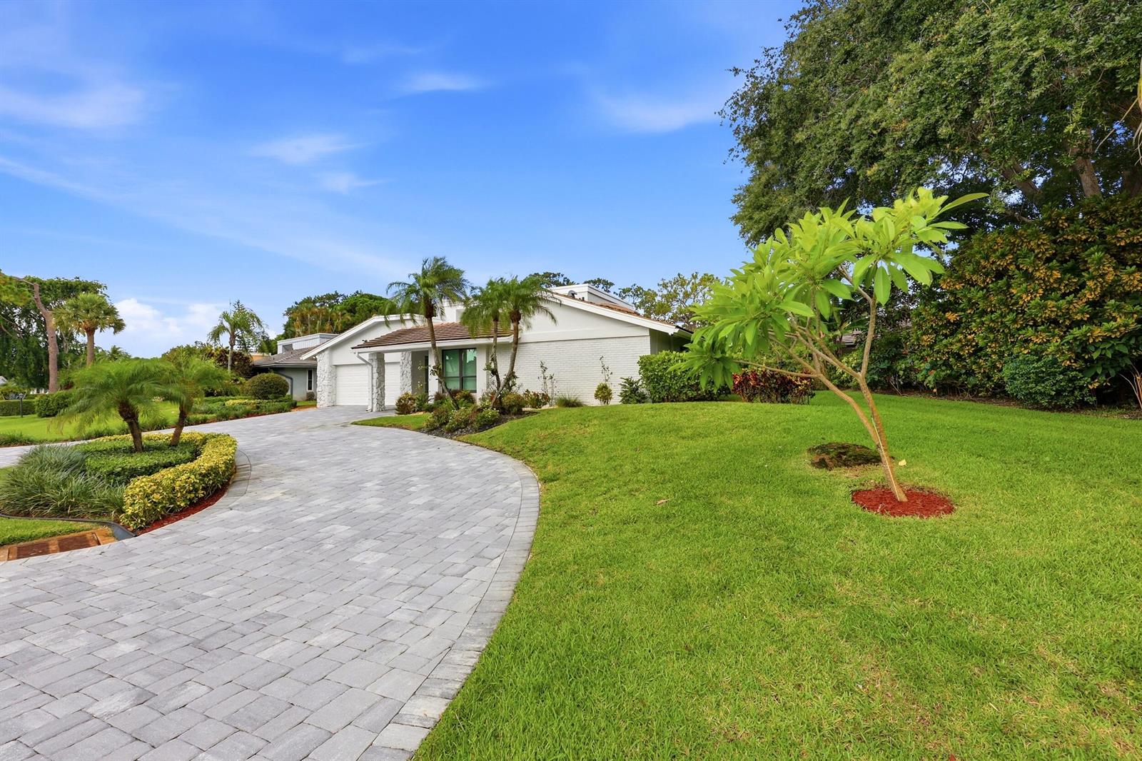 A white brick house with a paved driveway and landscaped lawn under a blue sky — 624 W Lakewoode Circle W, Delray Beach FL 33445, DELRAY BEACH, FL