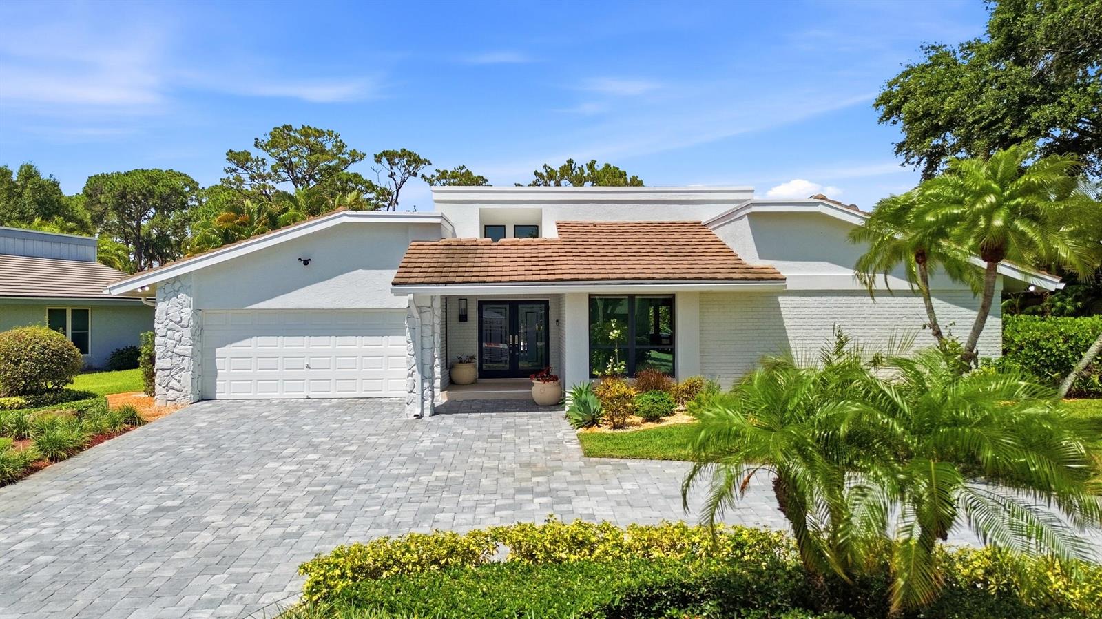 A white house with a brown tiled roof, stone accents, and a gray paver driveway — 624 W Lakewoode Circle W, Delray Beach FL 33445, DELRAY BEACH, FL