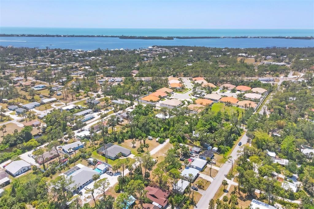 An aerial view shows a residential neighborhood with houses, lush trees, and a distant coastline — 521 ARTISTS AVENUE, ENGLEWOOD, FL