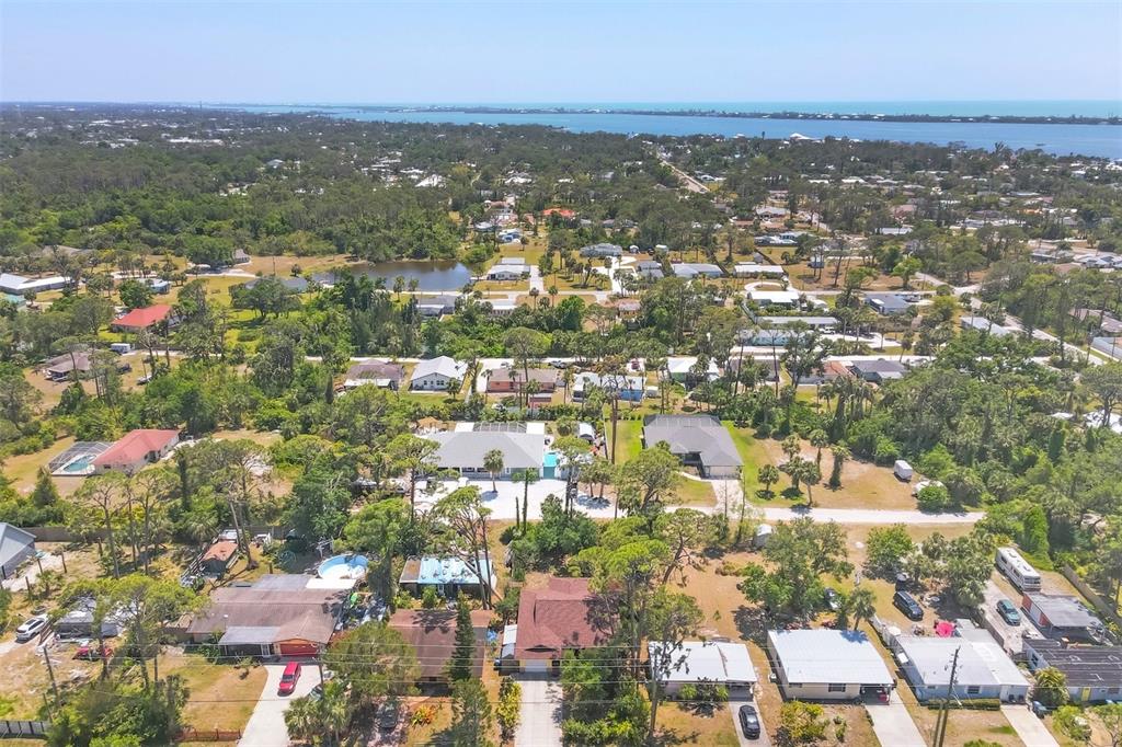 An aerial view shows a residential neighborhood with many trees, houses, and a distant bay — 521 ARTISTS AVENUE, ENGLEWOOD, FL