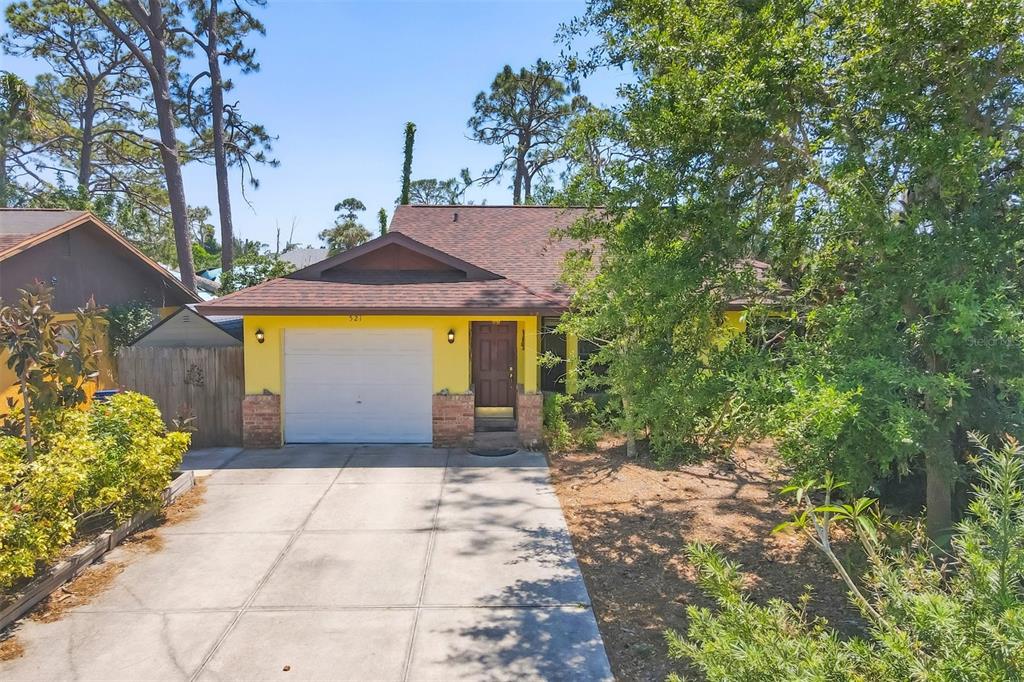 A yellow house with a brown roof, a single-car garage, and a concrete driveway — 521 ARTISTS AVENUE, ENGLEWOOD, FL
