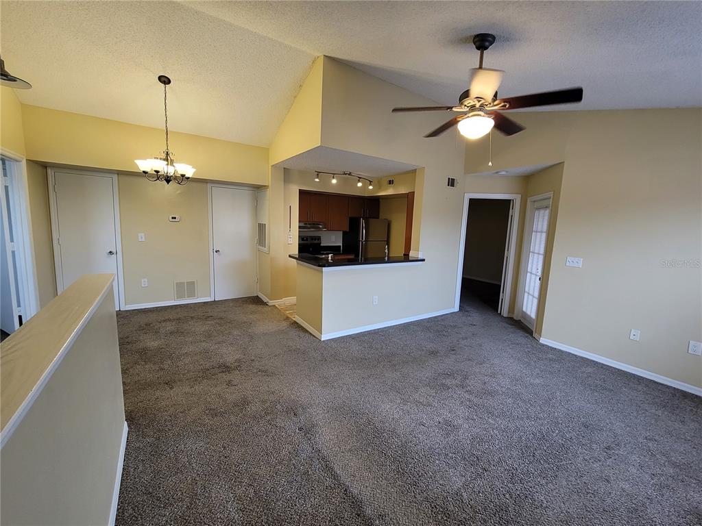 A living room with beige walls, brown carpet, a ceiling fan, and an open kitchen — 421 FOUNTAINHEAD CIRCLE UNIT 213, KISSIMMEE, FL