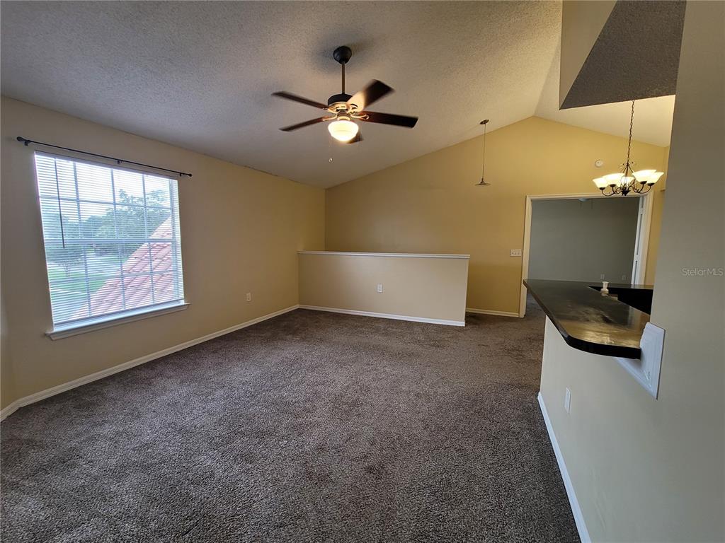 A carpeted living room features a vaulted ceiling, a ceiling fan, and a breakfast bar — 421 FOUNTAINHEAD CIRCLE UNIT 213, KISSIMMEE, FL