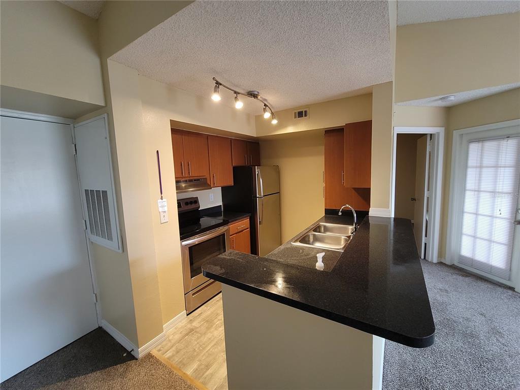A kitchen features dark countertops, wood cabinets, stainless steel appliances, and a breakfast bar — 421 FOUNTAINHEAD CIRCLE UNIT 213, KISSIMMEE, FL