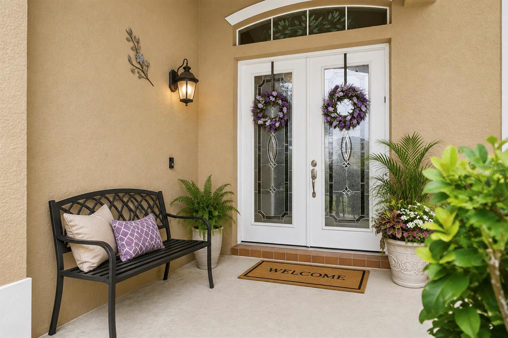 A covered entryway features a black metal bench, double glass doors with wreaths, and potted plants — 2648 VALIANT DRIVE, CLERMONT, FL
