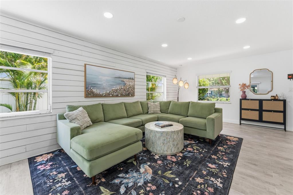 A living room features a green sectional sofa, a patterned rug, and white shiplap walls — 2701 67TH WAY N, ST PETERSBURG, FL