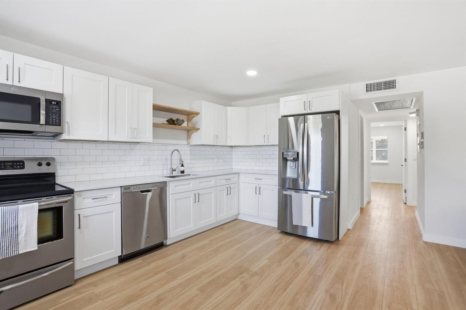 A modern kitchen features white cabinets, stainless steel appliances, subway tile backsplash, and light wood flooring — 2005 Newport G, Deerfield Beach FL 33442, DEERFIELD BEACH, FL