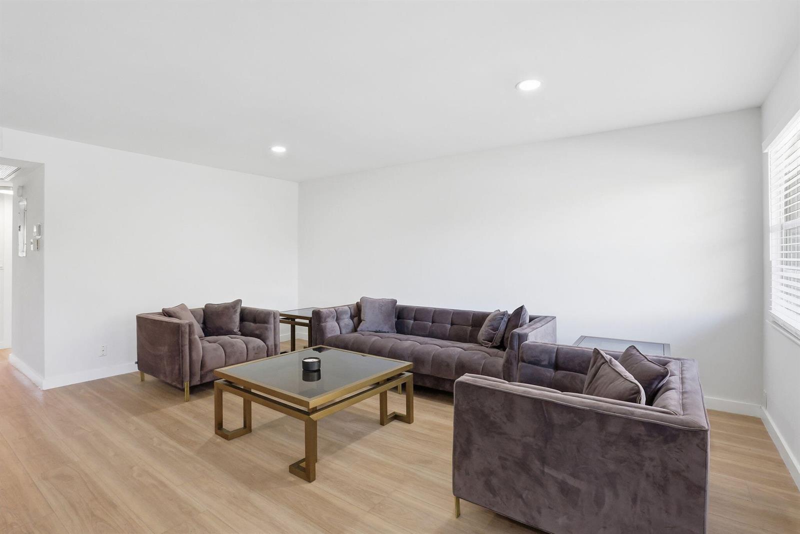 A living room features light wood flooring, white walls, and a dark velvet furniture set — 2005 Newport G, Deerfield Beach FL 33442, DEERFIELD BEACH, FL