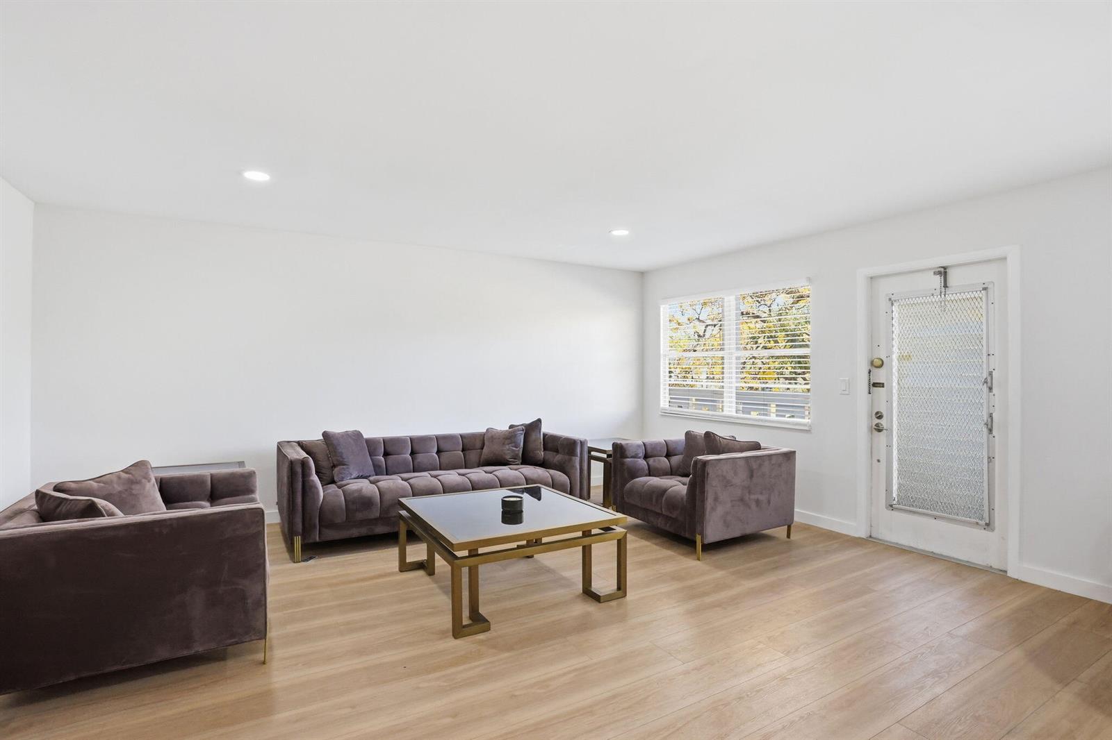 A living room features a dark velvet sofa set, a glass coffee table, and light wood flooring — 2005 Newport G, Deerfield Beach FL 33442, DEERFIELD BEACH, FL