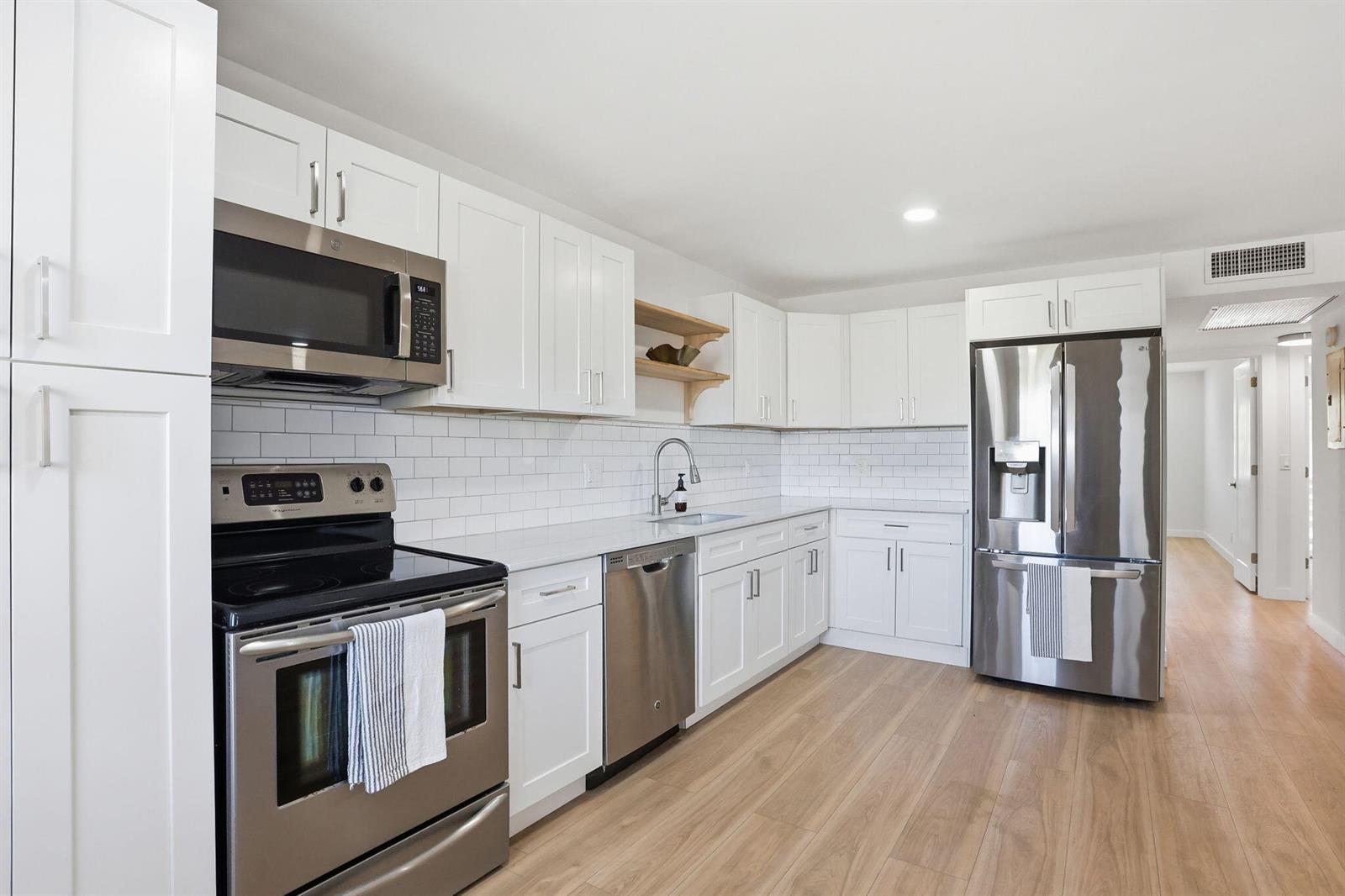 A modern kitchen features white cabinets, stainless steel appliances, white subway tile, and light wood flooring — 2005 Newport G, Deerfield Beach FL 33442, DEERFIELD BEACH, FL